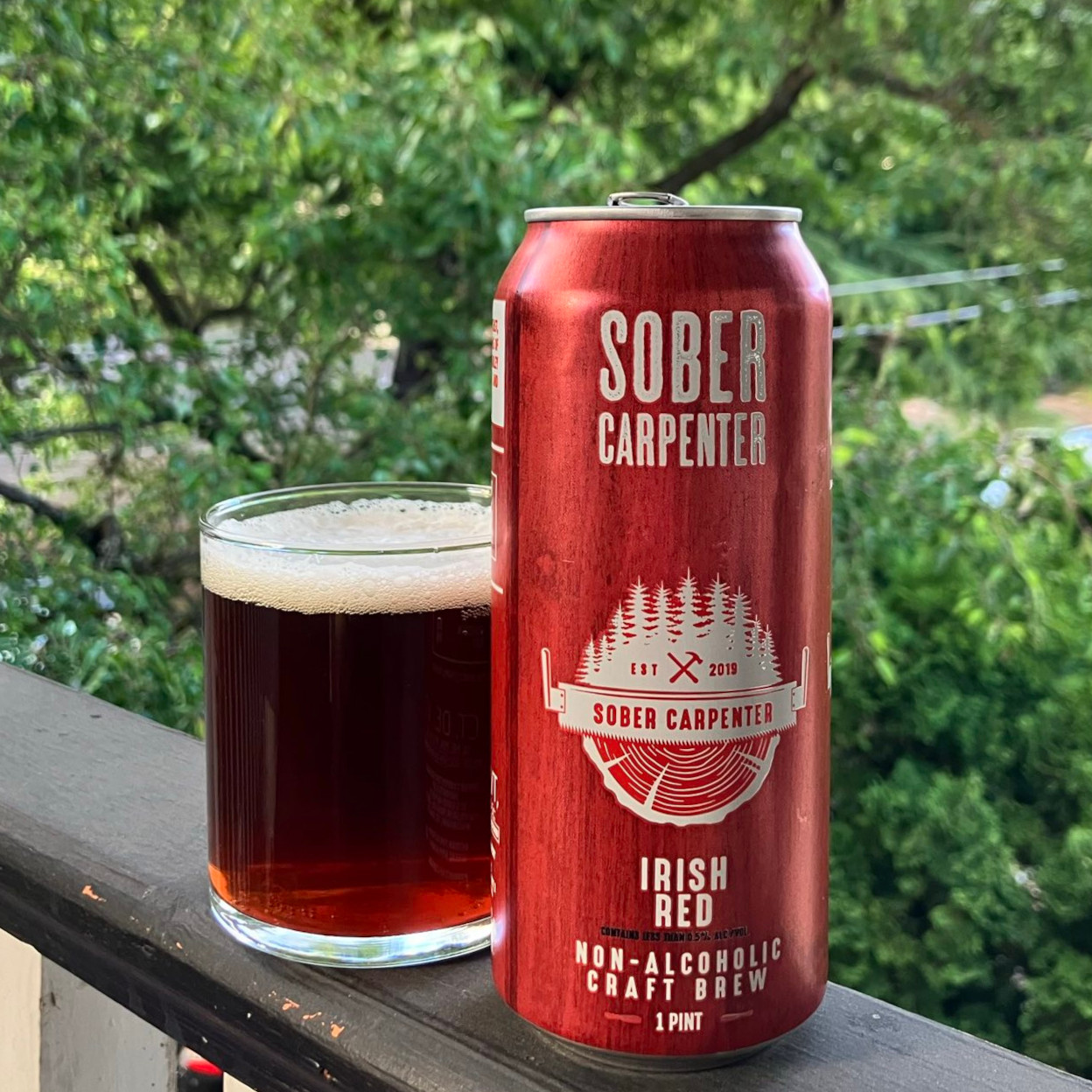 Sober Carpenter&rsquo;s Irish Red in a pint can, poured into a minimalist lowball glass, on a balcony railing